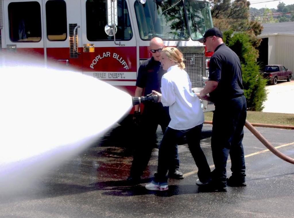 Firefighters Jeremy Downing [left] and David Dudley assist junior Jordan Rothenberger as she feels the force of a large diameter fire hose