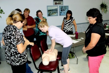 Teacher Bethany Noles of the 5th & 6th Grade Center applies chest compressions on a mannequin while a group of co-workers look on.