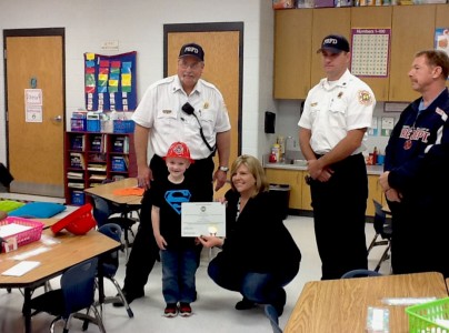Poplar Bluff Mayor Angela Pearson presents Hunter Schmidt a bravery award while [from left] Chief Ralph Stucker, Capt. Kevin Edgar and firefighter Bob Caswell give the boy a fire hat and badge.